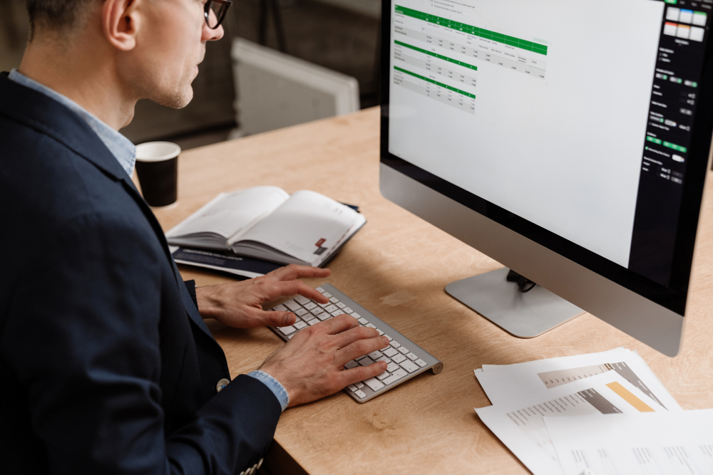Serious handsome man working with computer while sitting at table in office